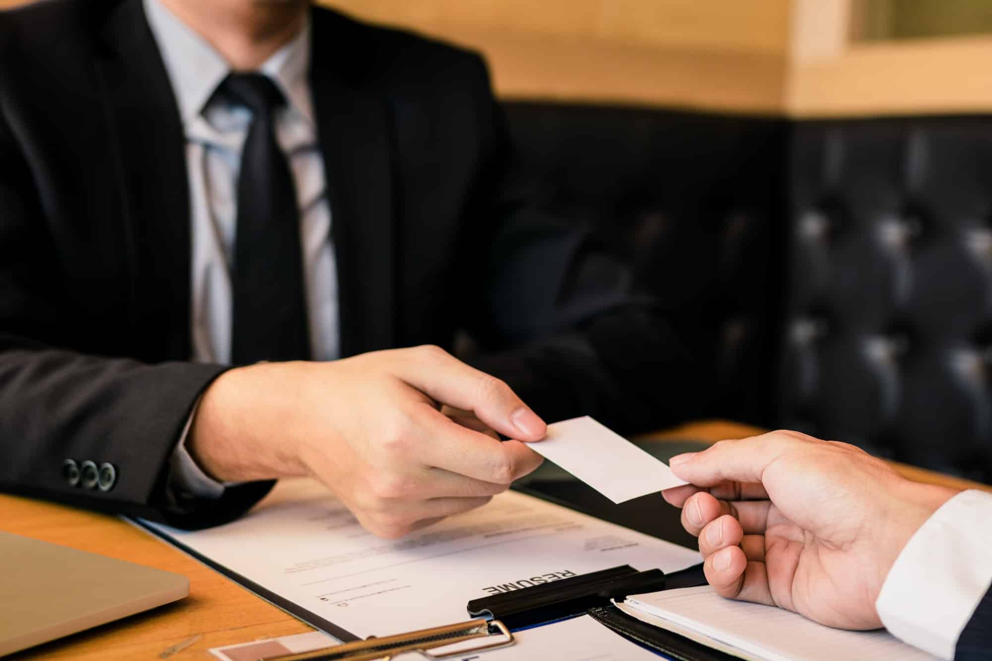 Two businessmen exchanged white business cards on a wooden table in office.